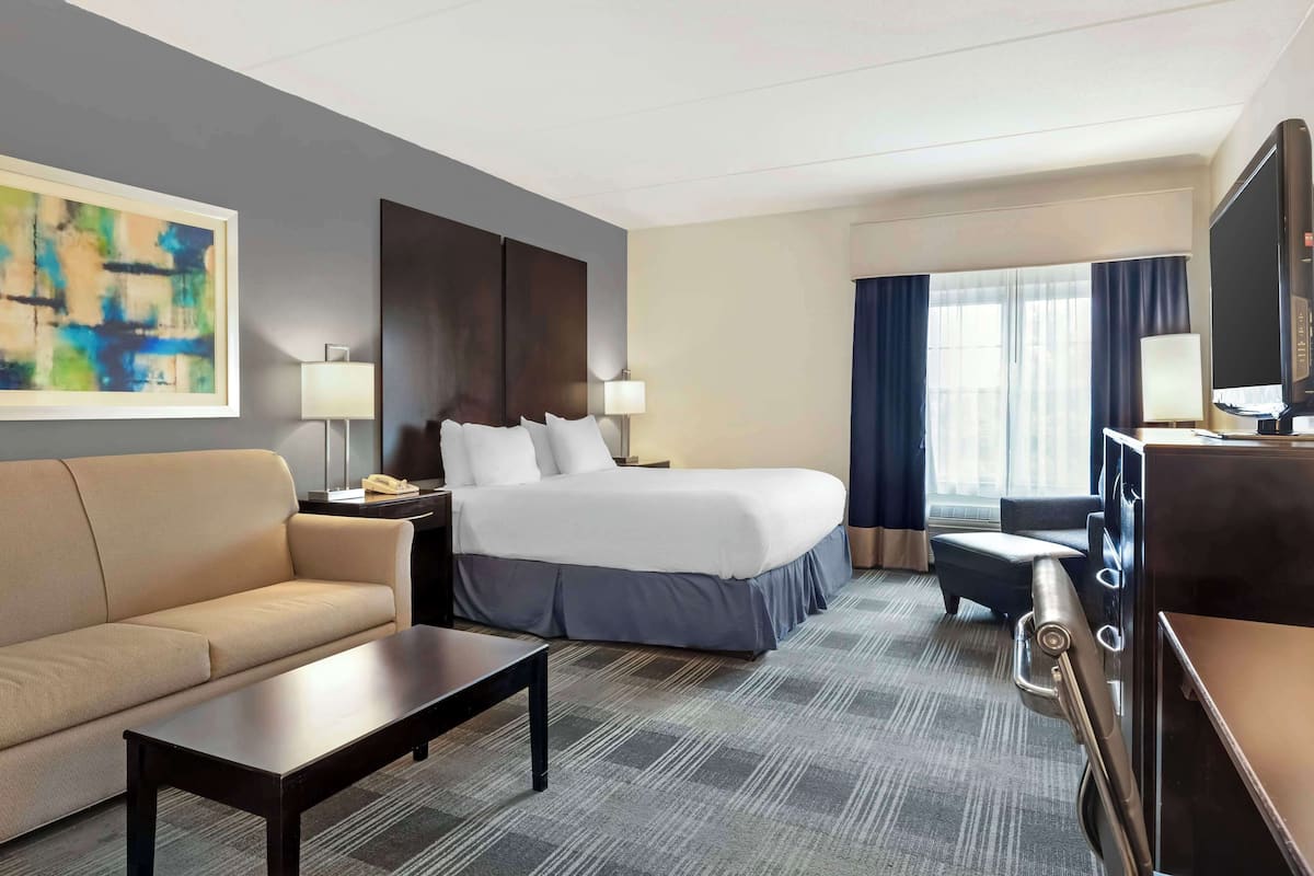 Ein Hotelzimmer mit Bett, Sofa, Schreibtisch, Fernseher und einem Bild an der Wand.