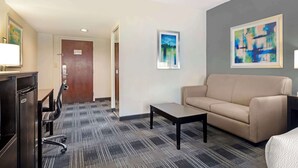Habitación de hotel con sofá, una mesita, escritorio con silla y un cuadro en la pared.