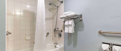 A bathroom with a bathtub, shower, and handrails.