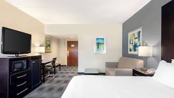 A hotel room with a large bed, a desk with a chair, a television, a desk lamp, and artwork on the walls.