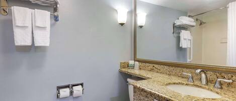 A bathroom with a granite countertop sink, a toilet, a towel rack with folded towels, a toilet paper holder, and a large mirror.