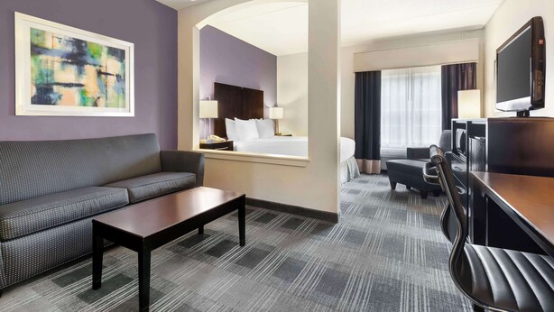 Habitación de hotel con sofá, mesa de centro, escritorio con silla, televisor y cama con cabecero.