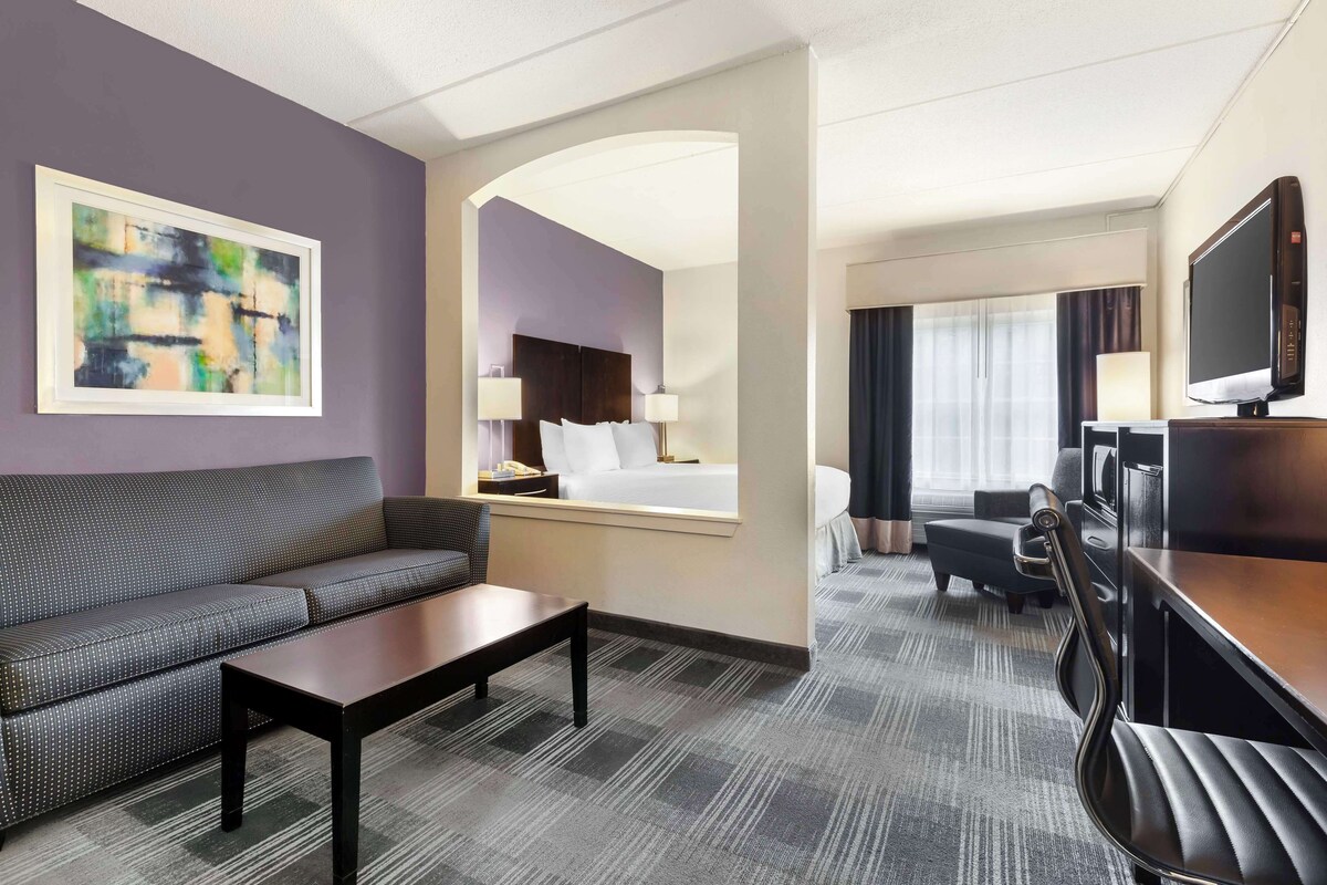 Une chambre d’hôtel comprenant un canapé, une table basse, un bureau avec une chaise, un téléviseur et un lit avec une tête de lit.
