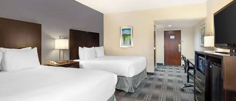 A hotel room with two beds, a desk with a computer, a TV, and a door leading to another room.
