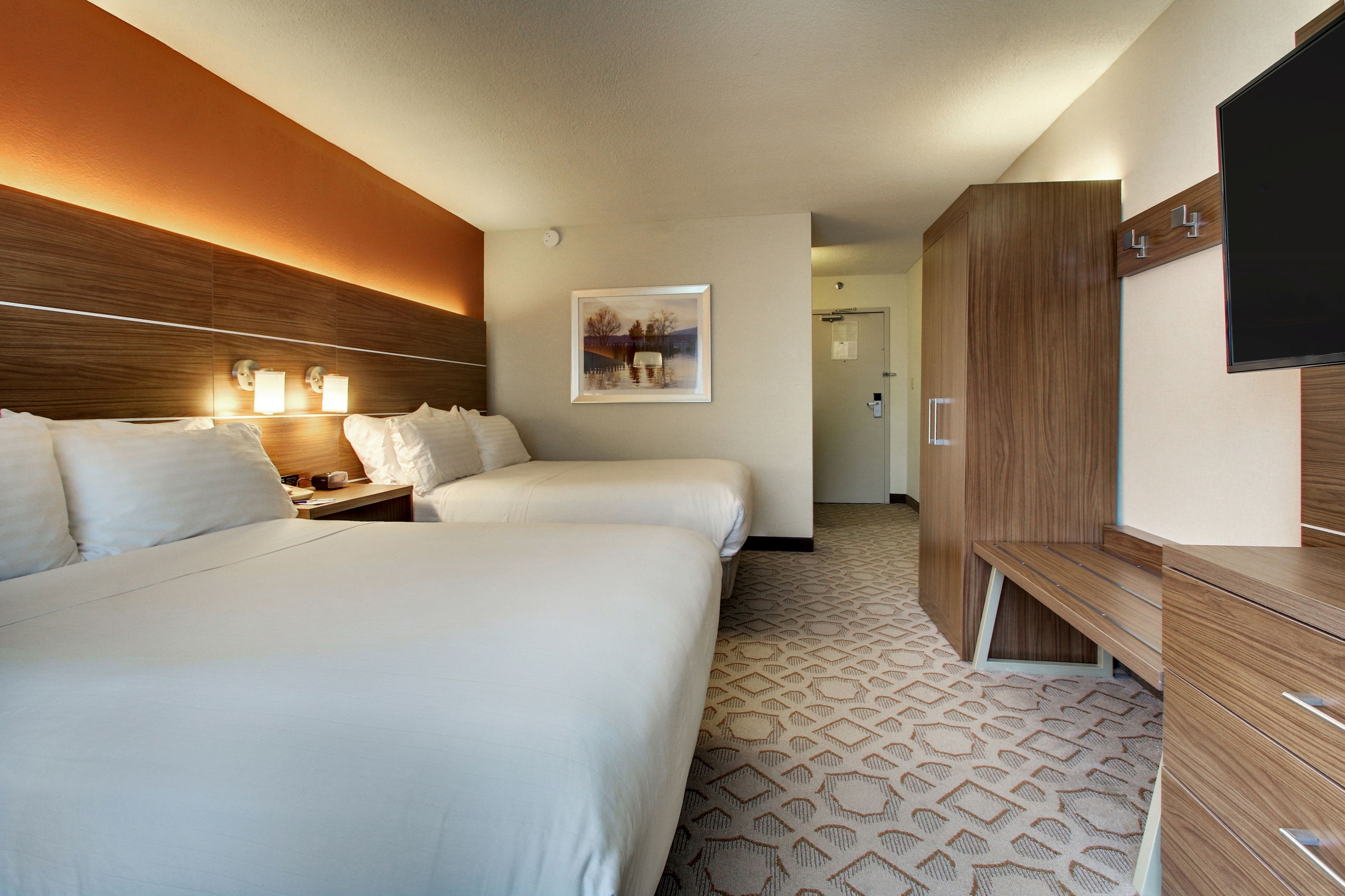 Habitación de hotel con dos camas, cabecero de madera, televisor de pantalla plana y alfombra estampada.