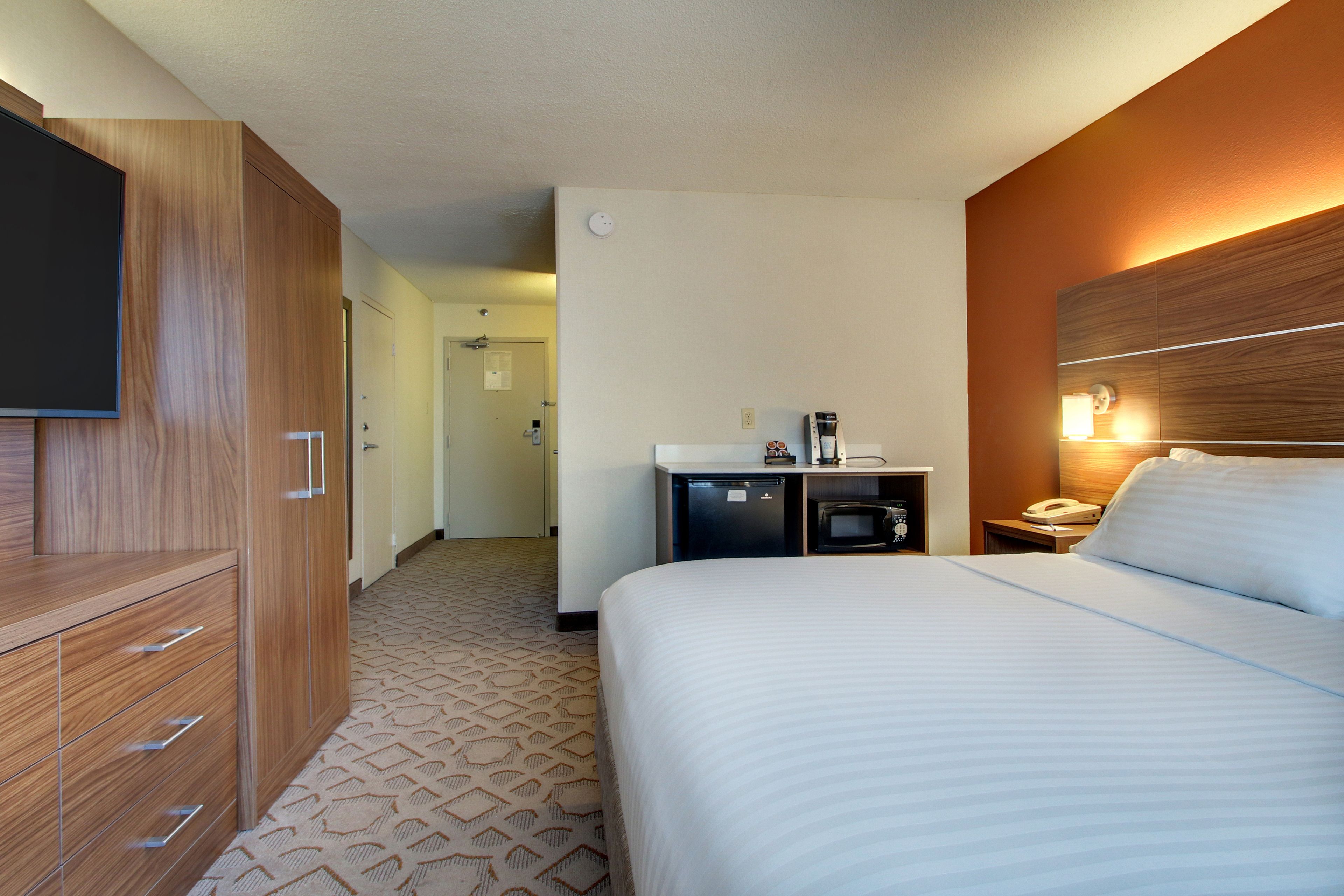 Une chambre d’hôtel avec un grand lit, une armoire en bois, un bureau avec un téléphone et un téléviseur fixé au mur.