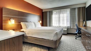 A hotel room with a bed, bedside tables, a desk, a chair, a TV, and a window with curtains.