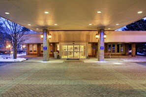 A hotel entrance with a brick facade, a glass door entrance, and a paved walkway.