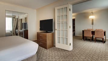 Una habitación de hotel con cama, televisión, escritorio y sillas, y una alfombra estampada.