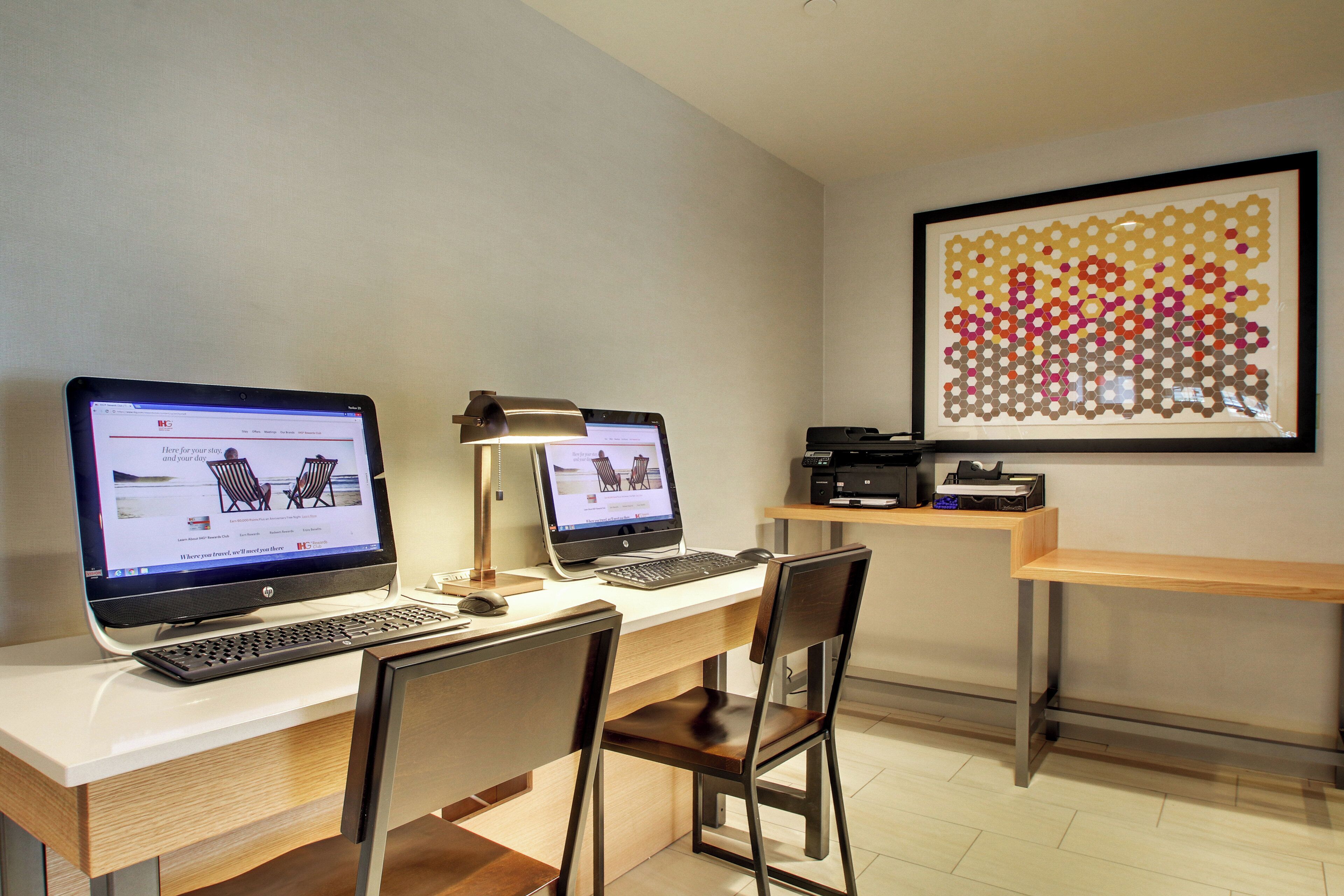 A workspace with two desktop computers, a desk lamp, and a framed artwork on the wall.