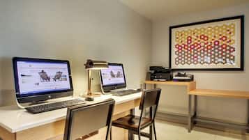 A workspace with two desktop computers, a desk lamp, and a framed artwork on the wall.