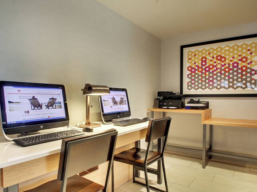 A workspace with two desktop computers, a desk lamp, and a framed artwork on the wall.