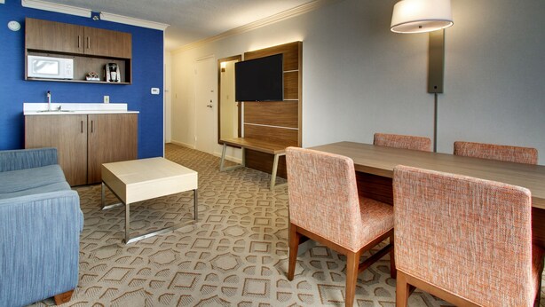 A modern living room with a dining area, a TV mounted on the wall, and a patterned carpet. - Holiday Inn Express Poughkeepsie by IHG (Poughkeepsie)