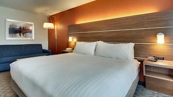 A hotel room with a large bed, a blue sofa, a nightstand with a lamp, and a framed picture on the wall.