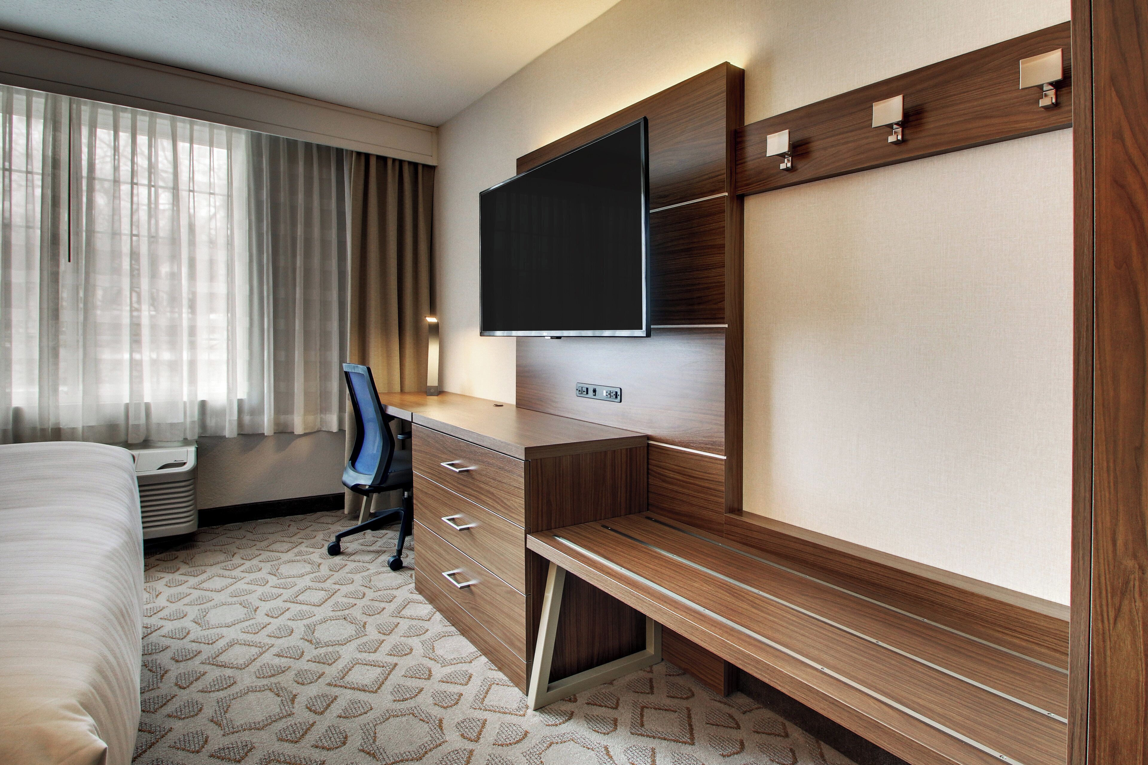 Een hotelkamer met een bed, een bureau met een flatscreen-televisie, een stoel en een vloerbedekking.