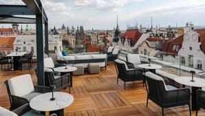 Une terrasse sur le toit, aménagée avec des meubles en osier, des tables rondes et offrant une vue sur un paysage urbain historique.
