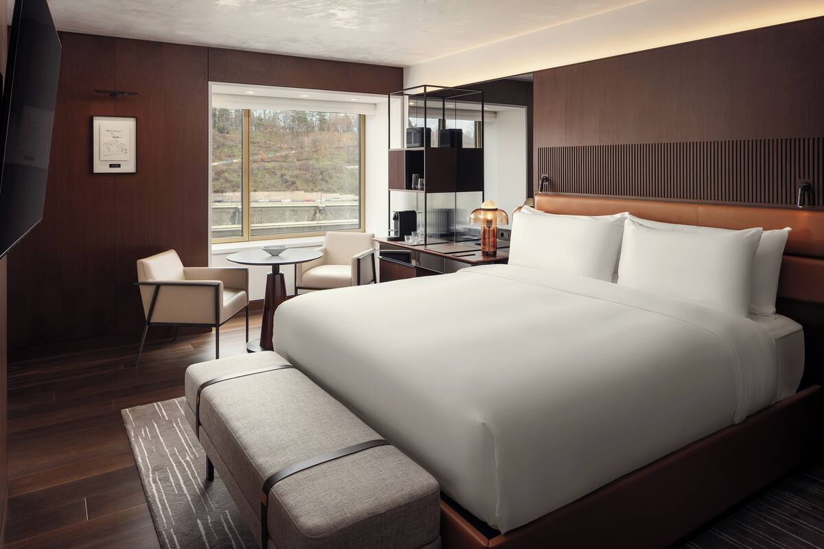 Una habitación de hotel moderna con una cama grande, un escritorio, una silla, una mesita y un ventanal con vistas al exterior.