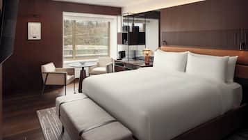Ein modernes Hotelzimmer mit einem großen Bett, einem Schreibtisch, einem Sessel, einem kleinen Tisch und einem großen Fenster mit Blick ins Freie.
