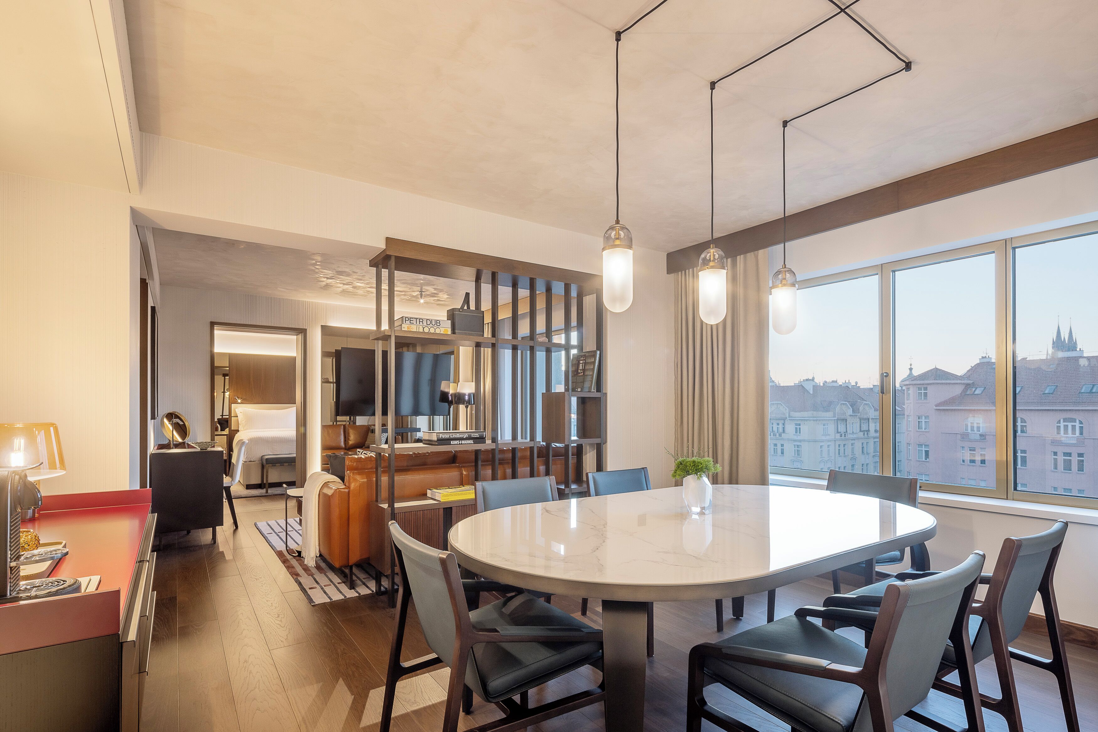 A modern hotel room with a large round table, comfortable seating, a television, and a city view.