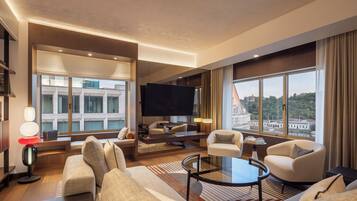 A modern hotel room with a large window, a flat-screen TV, and a seating area with sofas and a coffee table.