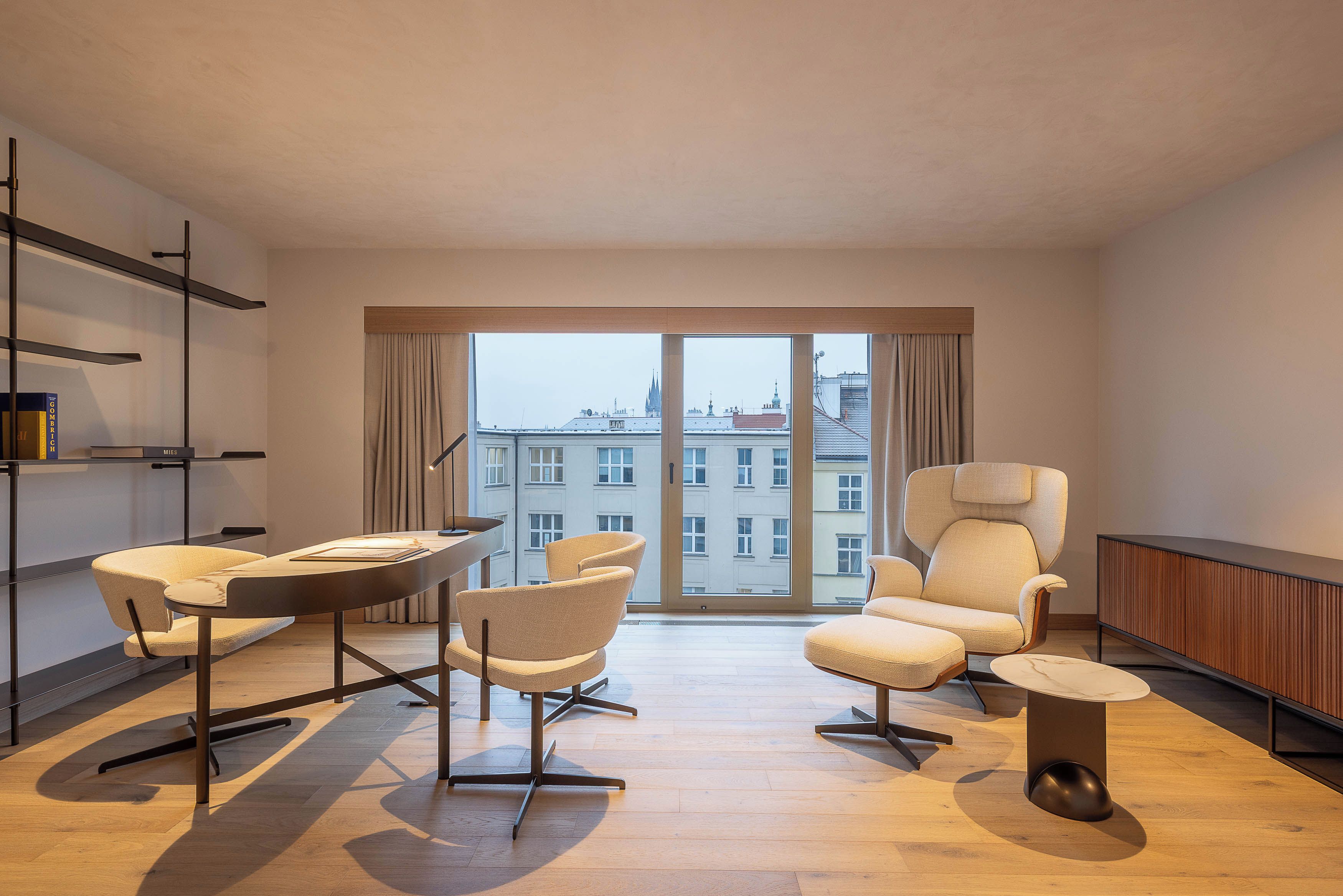 Un salon moderne avec une grande fenêtre, un canapé, un fauteuil, une petite table et une bibliothèque.