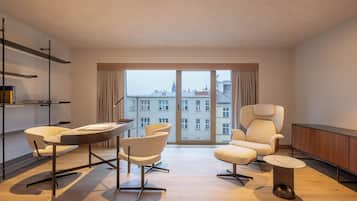 Un salon moderne avec une grande fenêtre, un canapé, un fauteuil, une petite table et une bibliothèque.