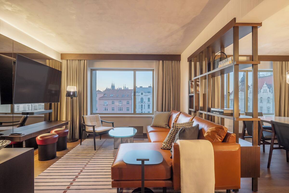 Una habitación de hotel moderna con un ventanal grande, un sofá, una mesa de comedor y una televisión.