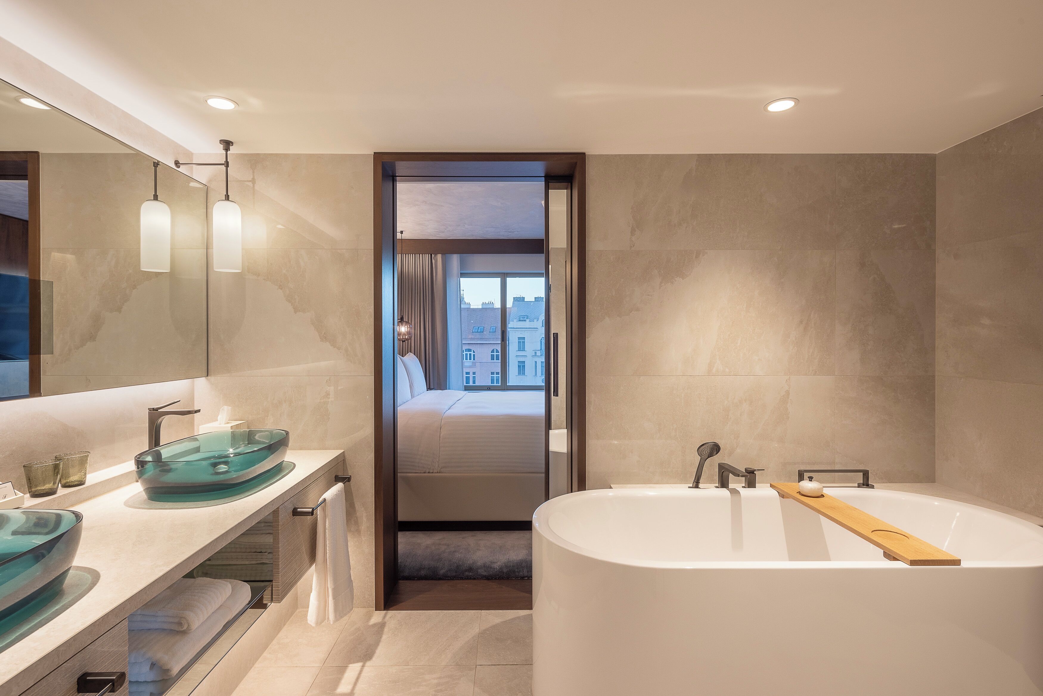 A modern bathroom with a glass sink, a large bathtub, and a view of a bedroom through a doorway.