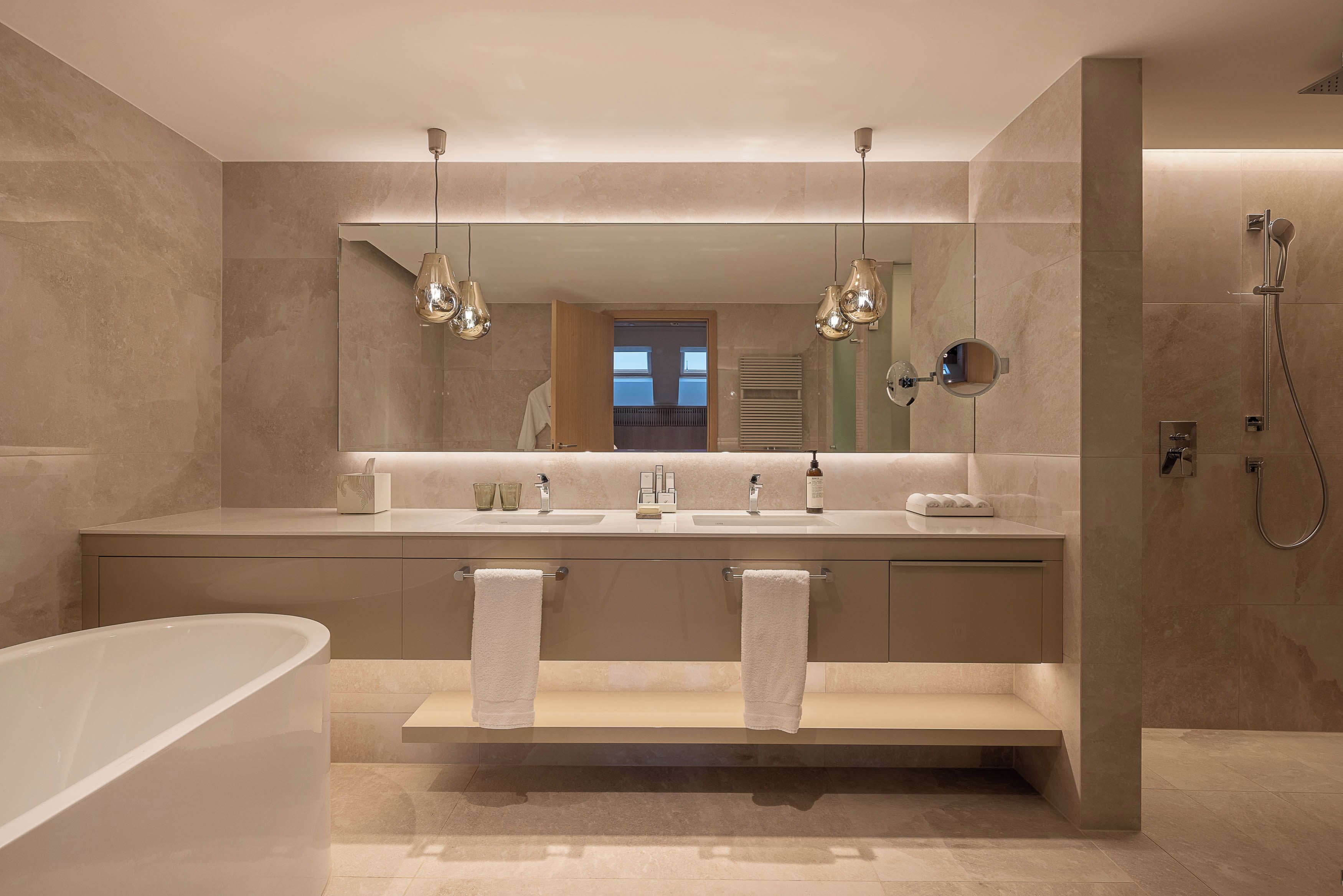 A modern bathroom with a bathtub, two sinks, a vanity, and a walk-in shower.