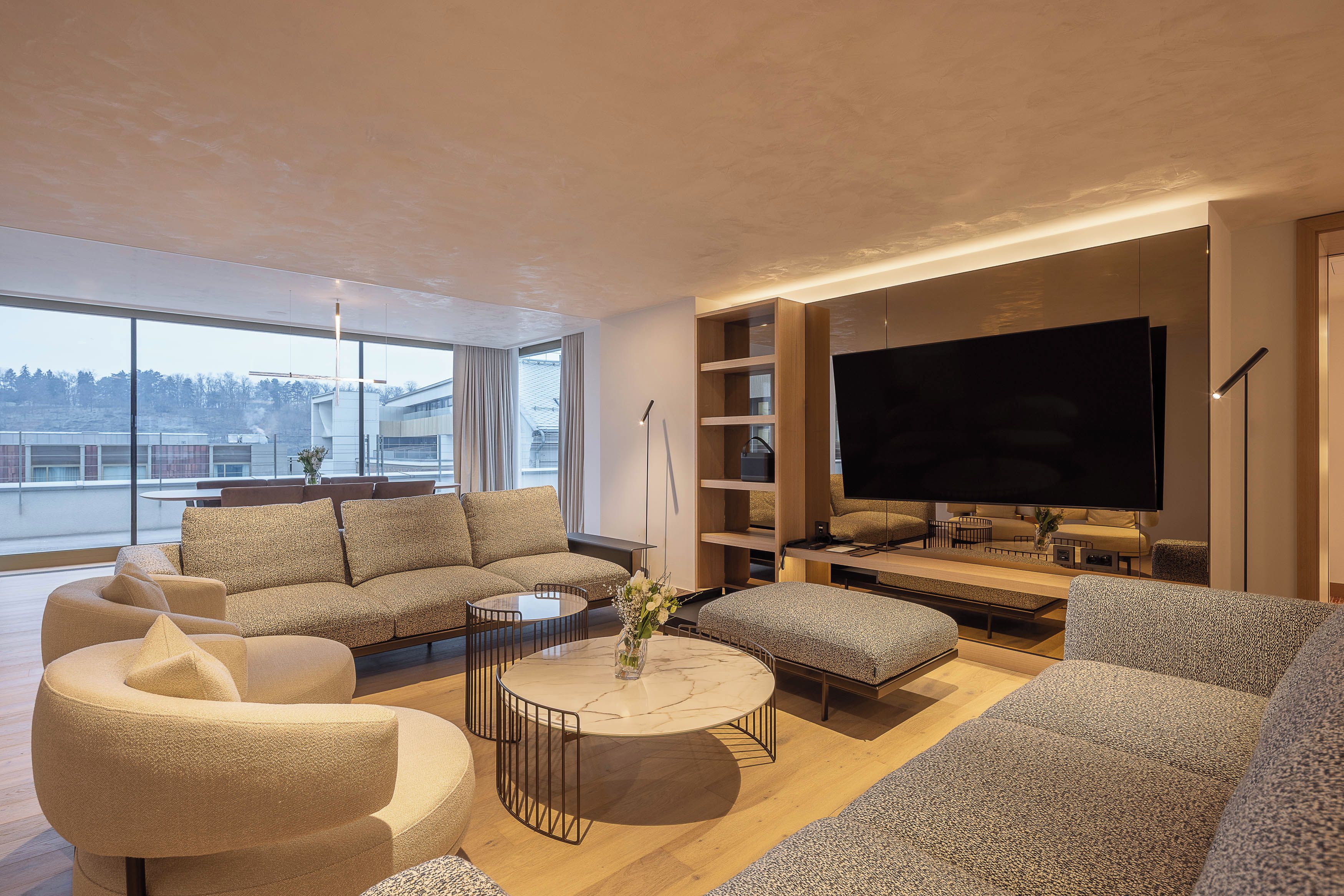 A modern living room with a large flat-screen TV, comfortable seating, and a view of the outdoors.