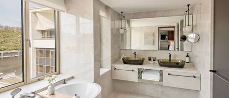 A modern bathroom with a large bathtub, two sinks, and a large mirror.