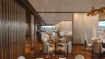 A modern dining area with high ceilings, a view of the city, and a mix of seating arrangements.