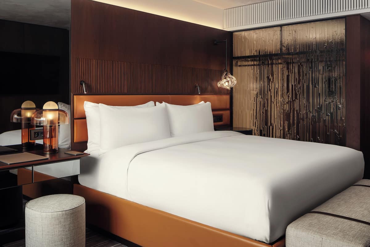 Una habitación de hotel moderna con una cama grande, un cabecero de madera, una mesita de noche con lámparas y un espejo amplio.