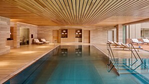 Une piscine intérieure moderne avec un plafond et des murs en bois, des chaises longues et une paroi en verre transparent.