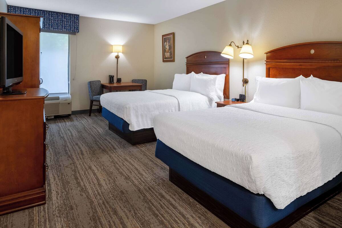 A hotel room with two beds, a desk, a chair, and a television.