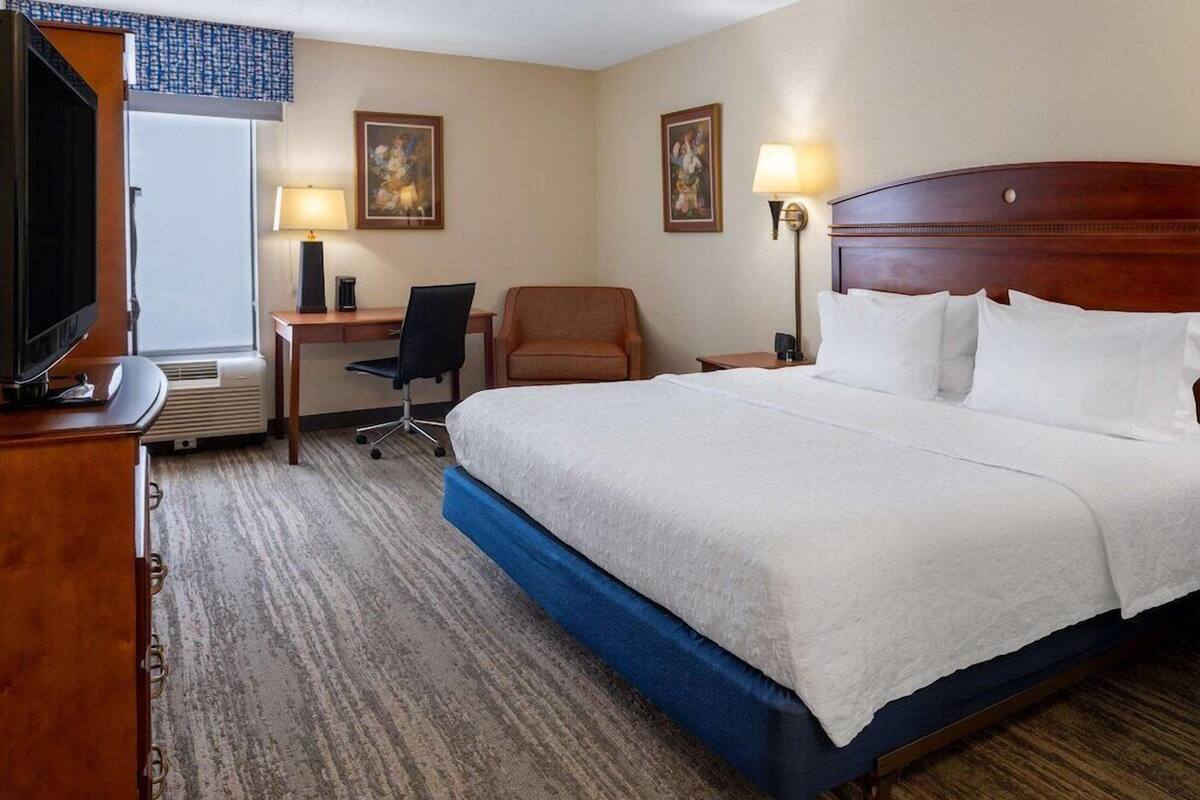 A hotel room with a large bed, a desk with a chair, a television, and two wall-mounted lamps.