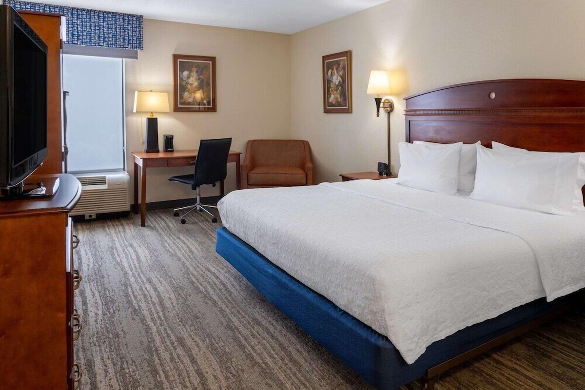 Une chambre d’hôtel avec un grand lit, un bureau avec une chaise, une télévision et deux lampes fixées au mur.