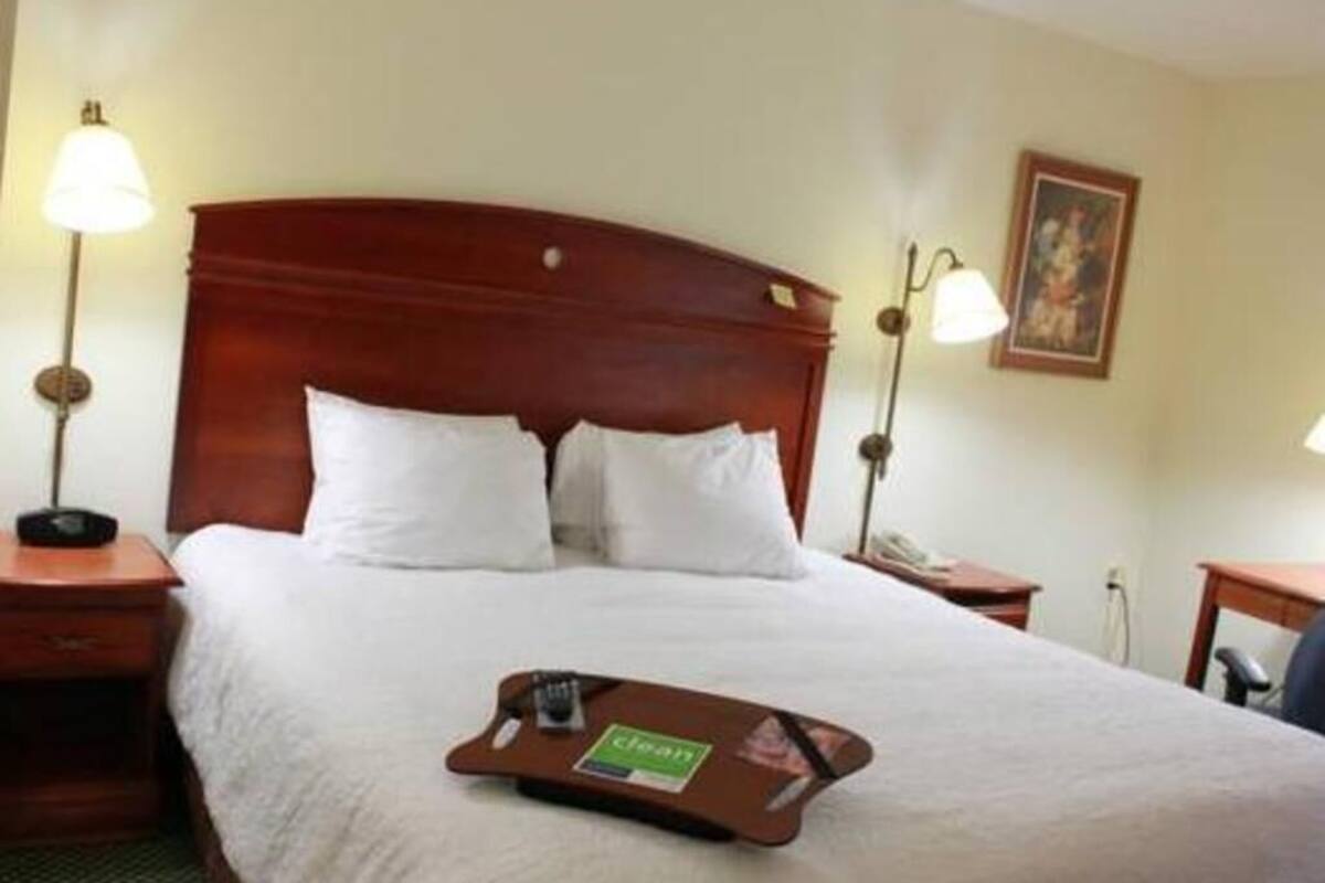 A hotel room with a large bed, two bedside lamps, a framed picture on the wall, and a tray with a 'clean' sign on the bed.