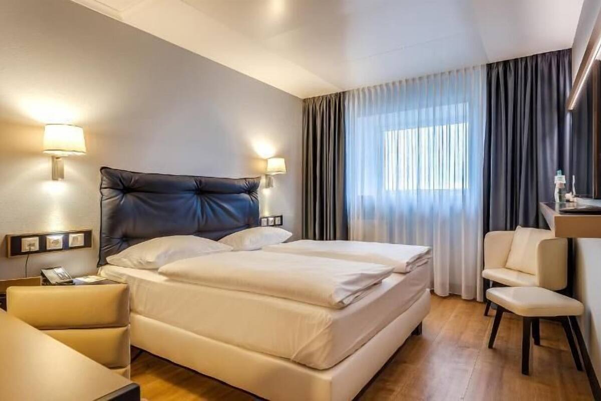 Une chambre d’hôtel comprenant un lit, des tables de chevet, un bureau, une chaise, une télévision et des rideaux.