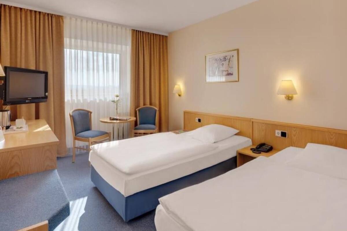 Et hotelværelse med to senge, et skrivebord, en stol, et fjernsyn og et lille bord.