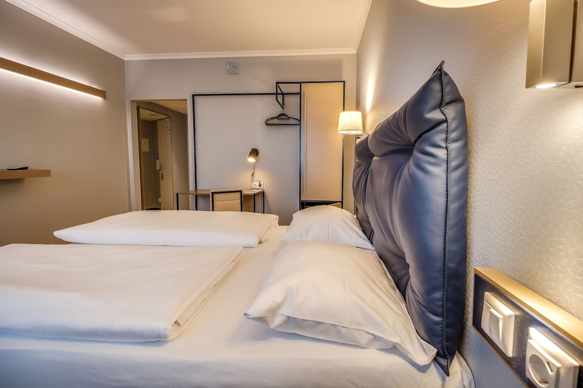 Et hotelværelse med to senge, et natbord med lampe og et spejl på væggen.
