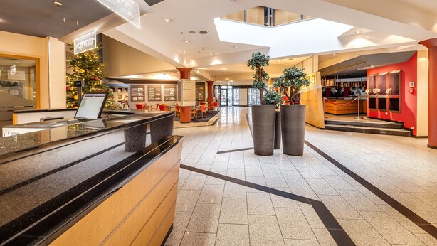 Un espace d’accueil d’hôtel au design moderne, comprenant un comptoir d’accueil, un sapin de Noël et une grande plante en pot.