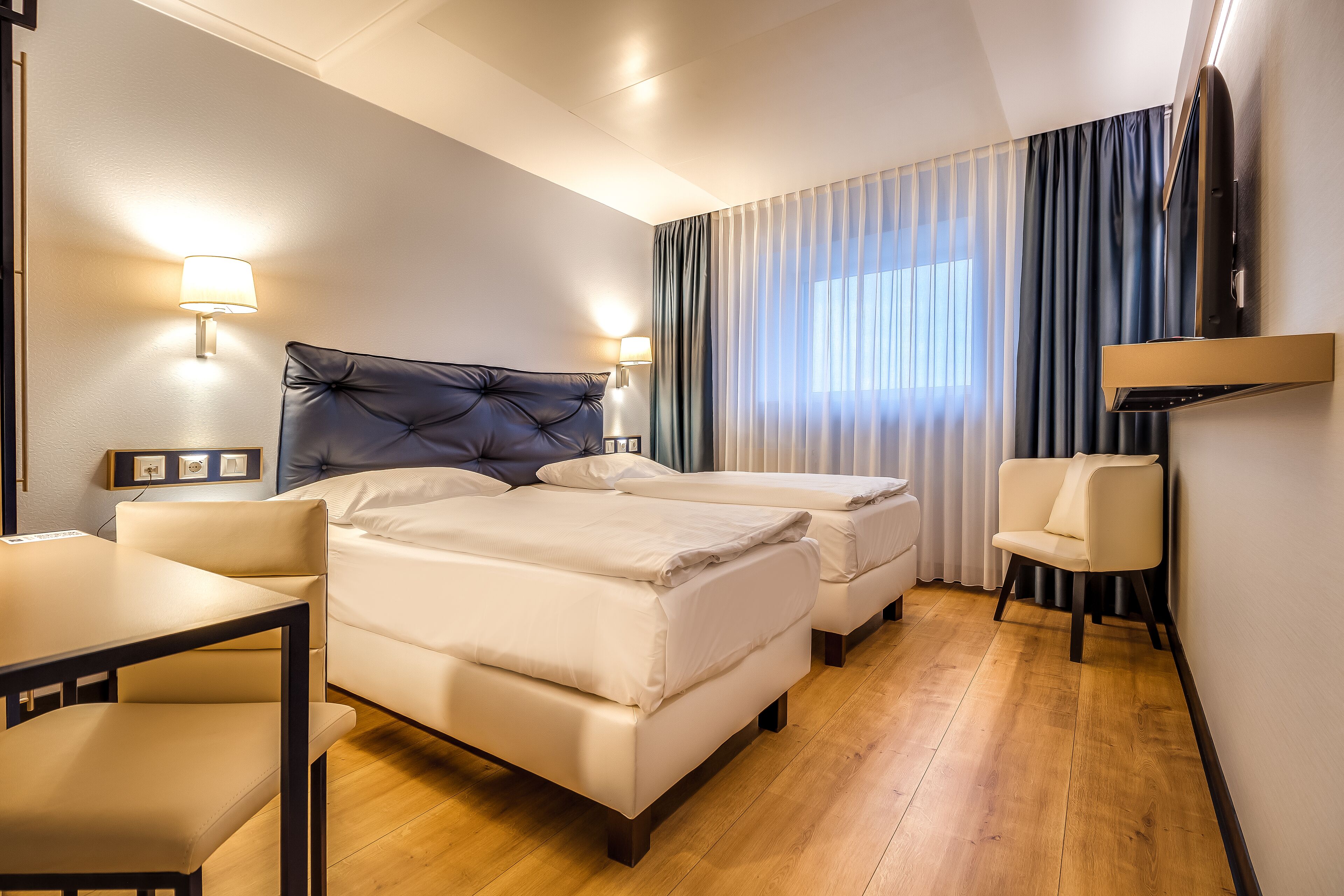A hotel room with a large bed, a smaller bed, a desk, and a chair.