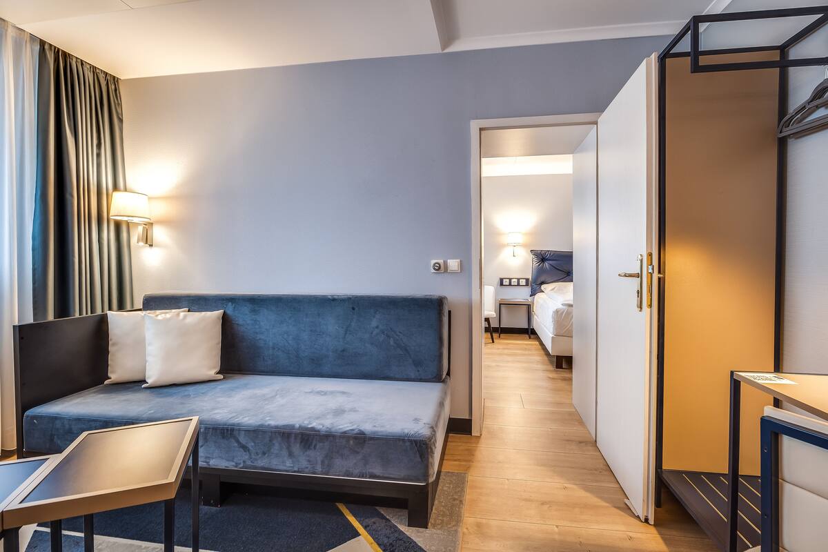 Et moderne hotelværelse med en blå sofa, et lille bord og en seng i baggrunden.
