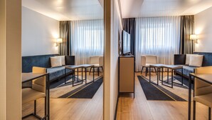 Une chambre d’hôtel moderne équipée d’un canapé, de deux fauteuils, d’une petite table, d’une télévision et d’un bureau.