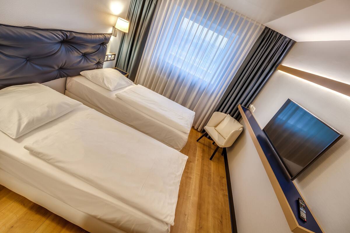Une chambre d’hôtel avec un grand lit, un lit plus petit, un bureau avec une télévision et une chaise.