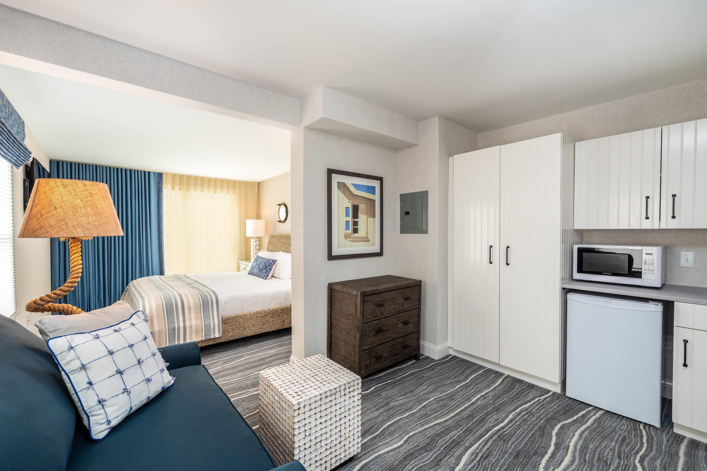 A hotel room with a bed, a sofa, a small table, a microwave, and cabinets.
