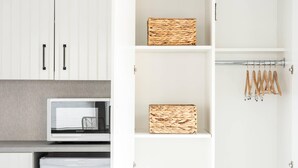A white wardrobe with two doors, a microwave, and shelves with woven baskets and wooden hangers. - Edgar Hotel Martha's Vineyard, an Ascend Collection Hotel (Edgartown)