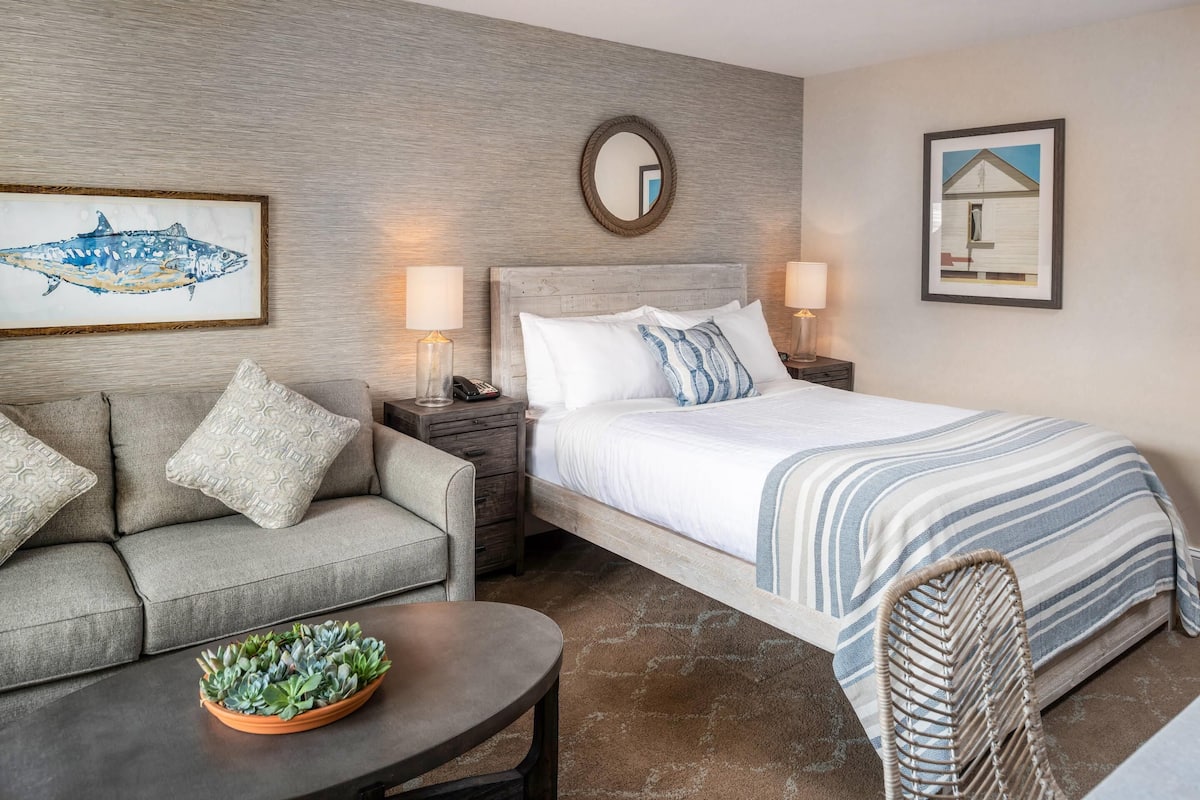A hotel room with a bed, a sofa, a chair, a nightstand, and a coffee table.