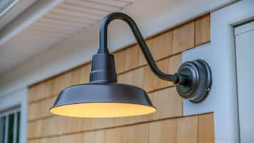 A wall-mounted outdoor light fixture with a curved arm and a round base.